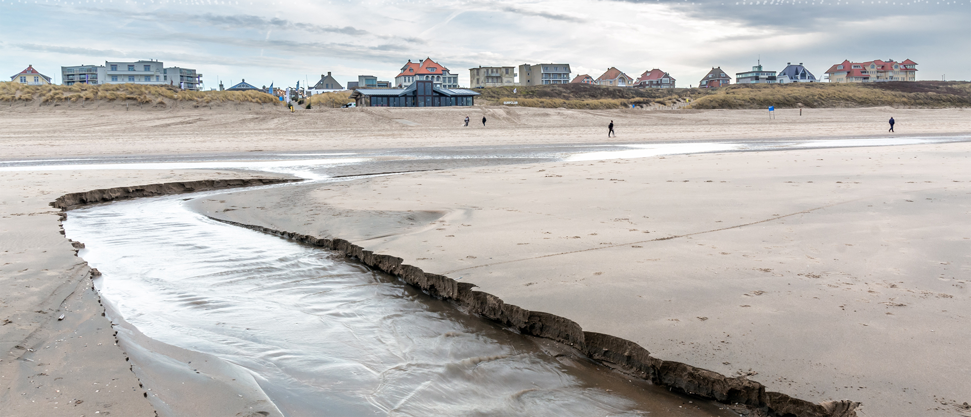 A beach with people walking on it and buildings in the background.