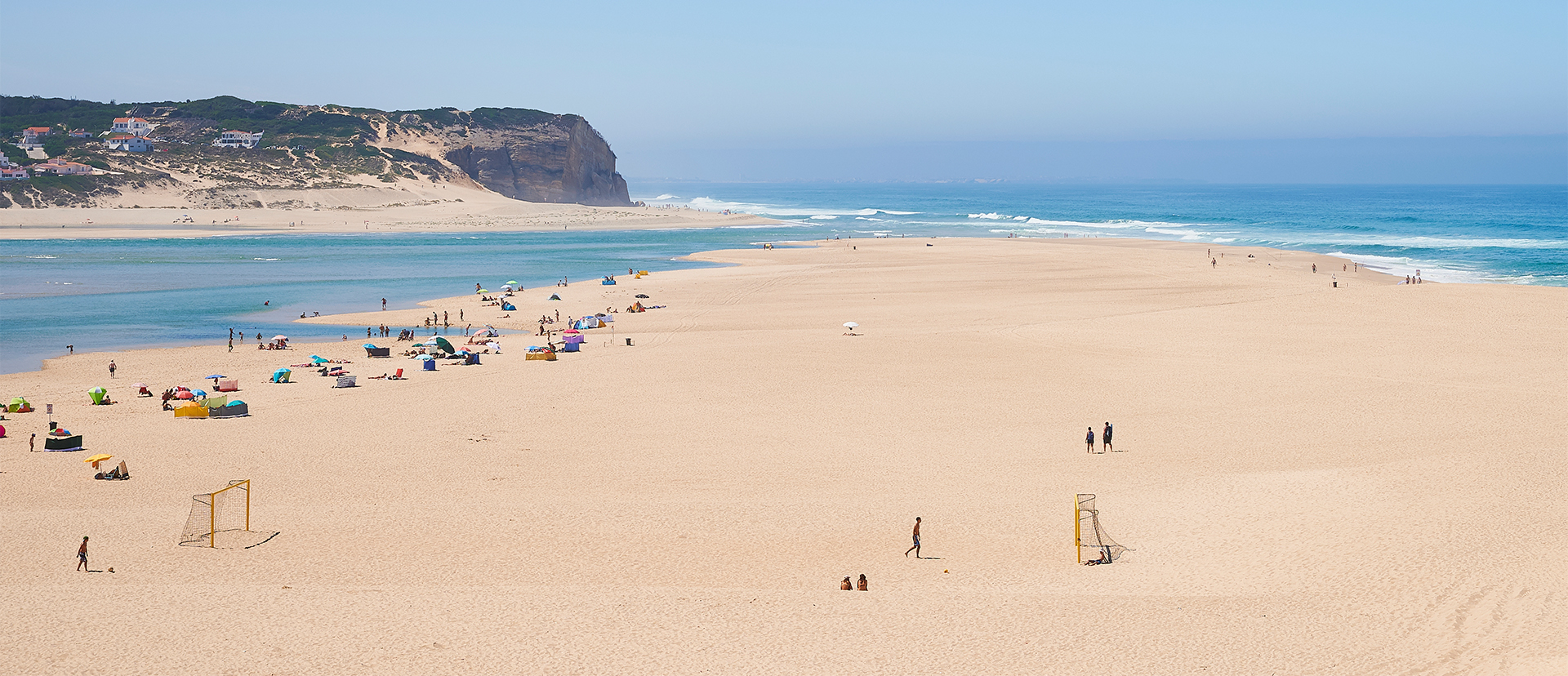 A beach with people walking and sitting on the sand.